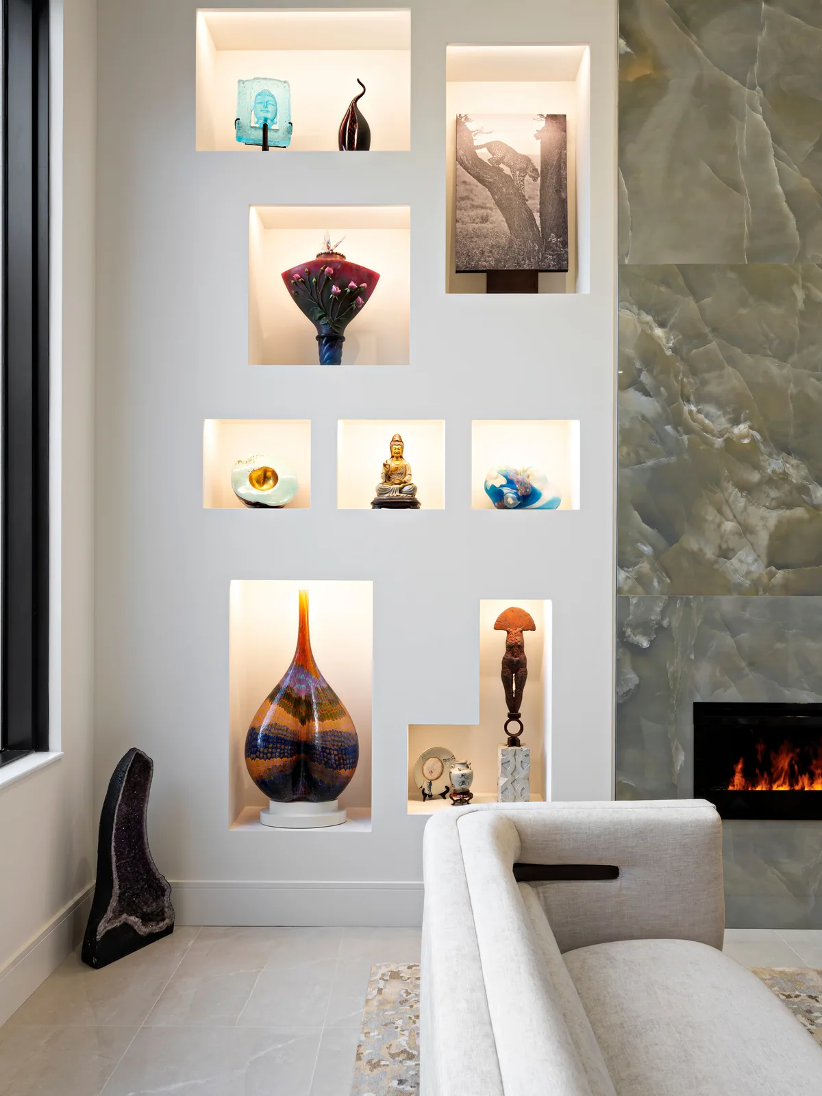Built-in display niche wall with lit recessed openings beside an onyx slab fireplace surround
