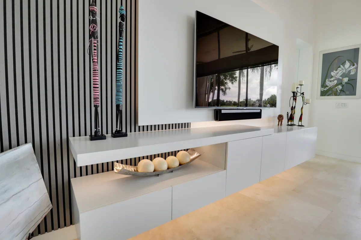 Contemporary media wall with a black slat wood feature panel and a long white floating credenza with a lit open niche, Palm Beach County residence, Jupiter FL